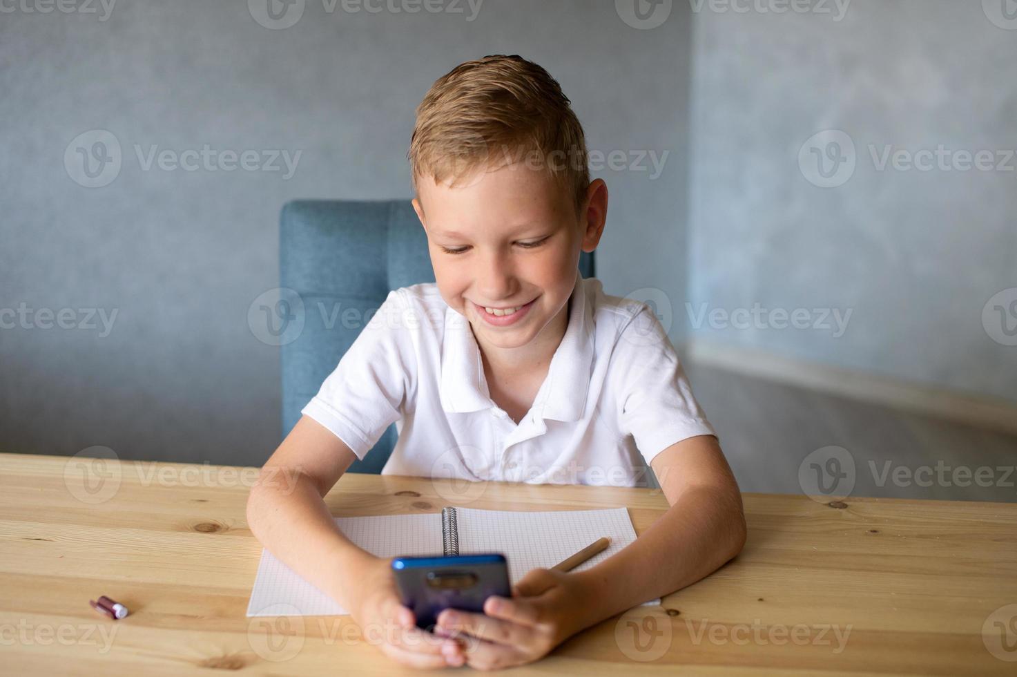 Cute boy writes in an open notebook and looks at the phone. photo
