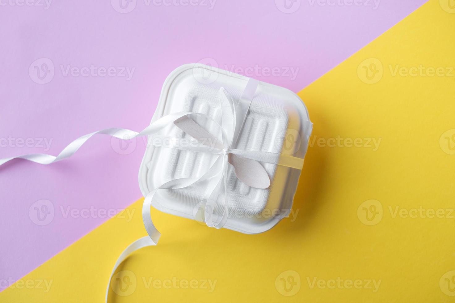 A small box with a wooden spoon tied with a white satin ribbon . Yellow and pink background photo