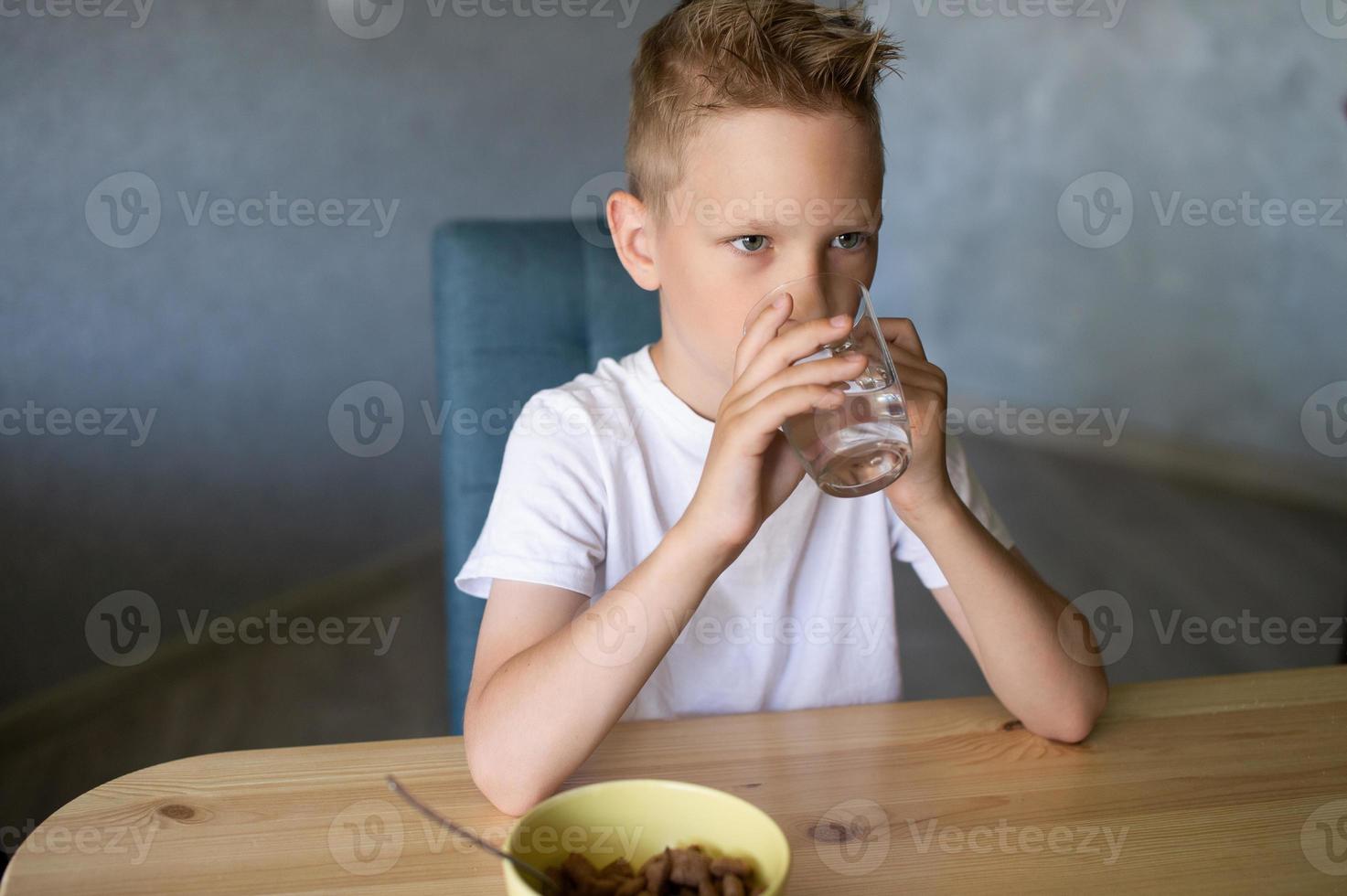 A cute boy drinks water and eats a dry breakfast at home and smiles photo