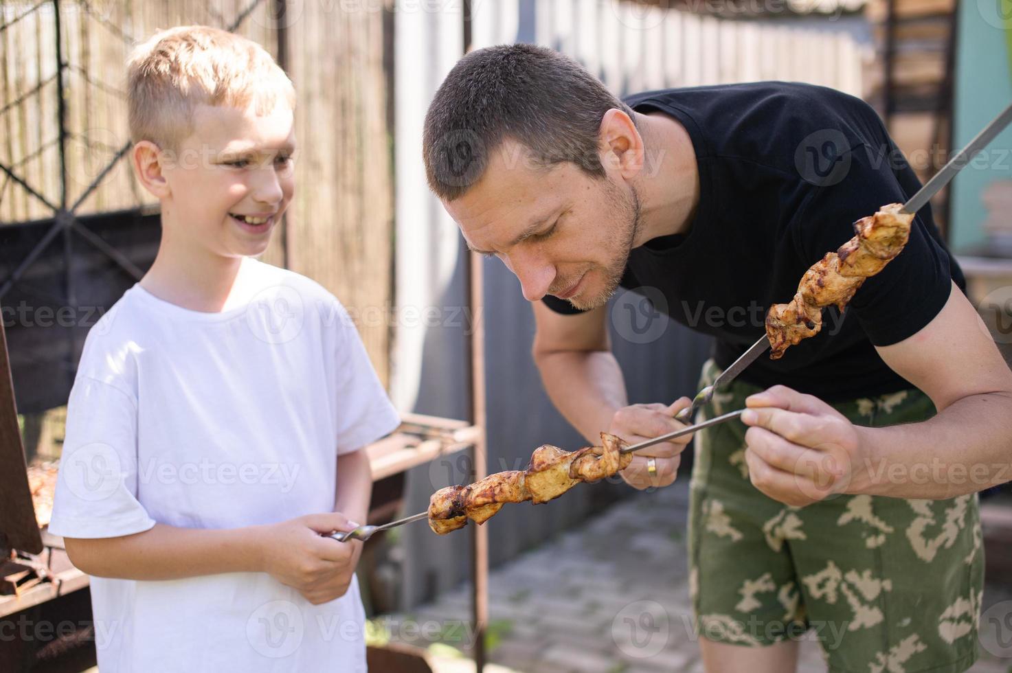 gracioso papá y hijo tratar A la parrilla carne foto