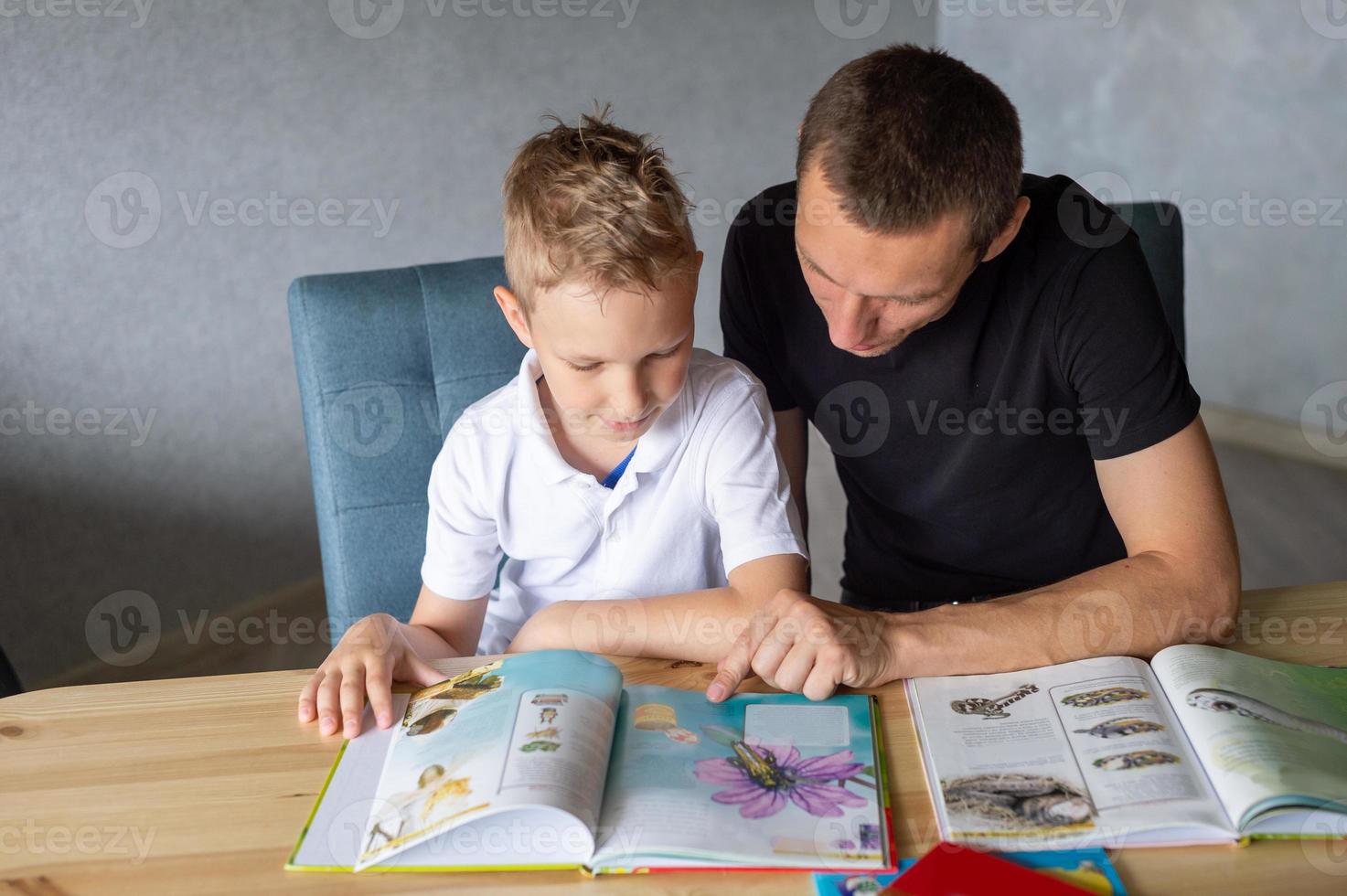 un linda chico es sentado a el mesa con su papá y acecho un libro acerca de mariposas foto