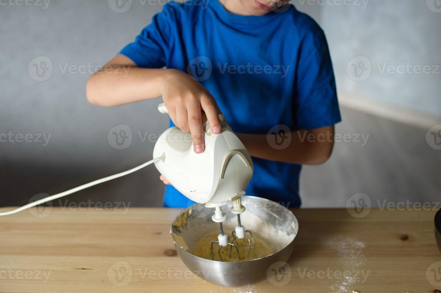 A child prepares dough in metal bowls. Lower the mixer into the bowl photo