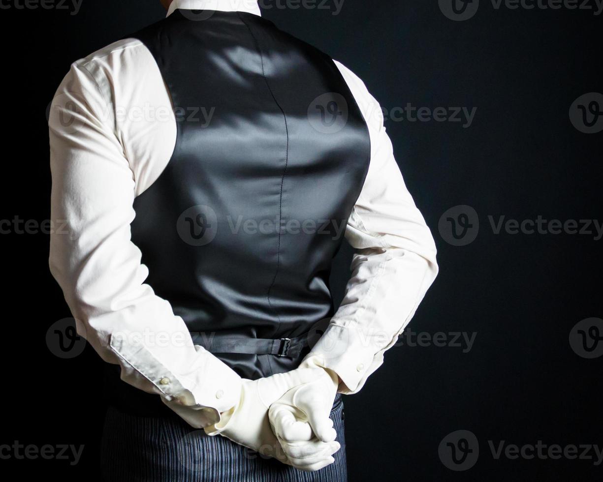 Portrait of Butler or Waiter in Vest and White Gloves Standing With Hands Behind Back in Respectful Attention. Service Industry and Professional Hospitality. photo