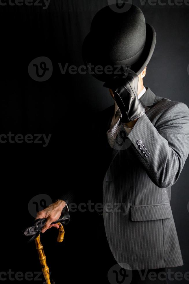 retrato de empresario en oscuro traje quitándose jugador de bolos sombrero en negro antecedentes. Clásico estilo y retro Moda de clásico Inglés Caballero. foto