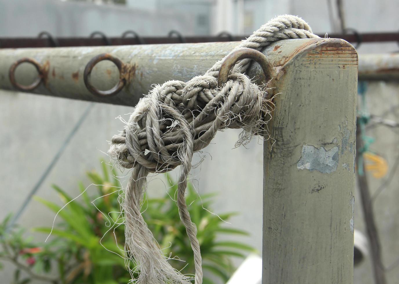 Loose unsafe white old rope thread tied up on steel fence. photo
