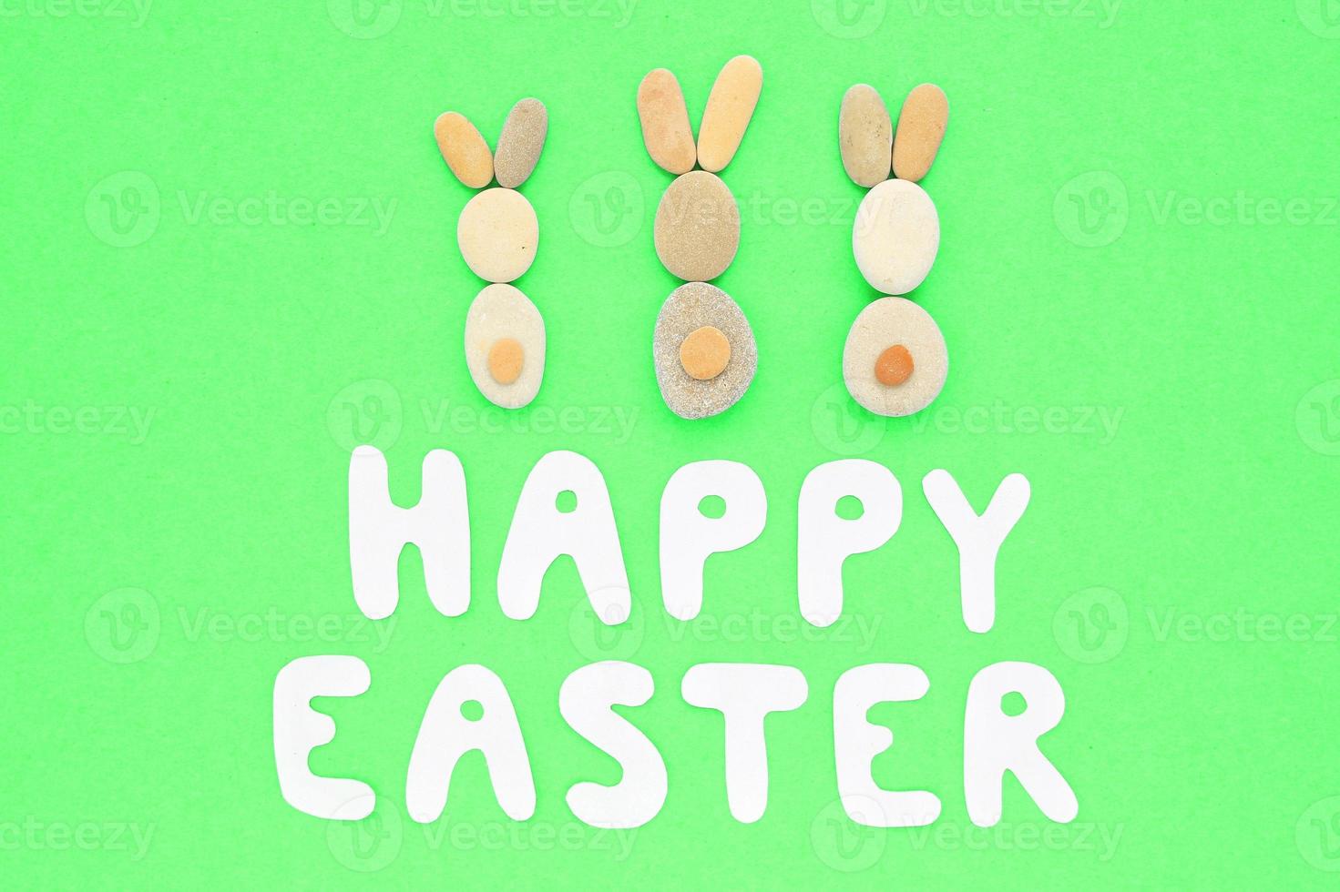 Happy Easter lettering and bunnies from pebbles on green background. Flatlay postcard creative concept. Creative greetings with natural craft ecological materials. Save the planet, zero waste idea. photo