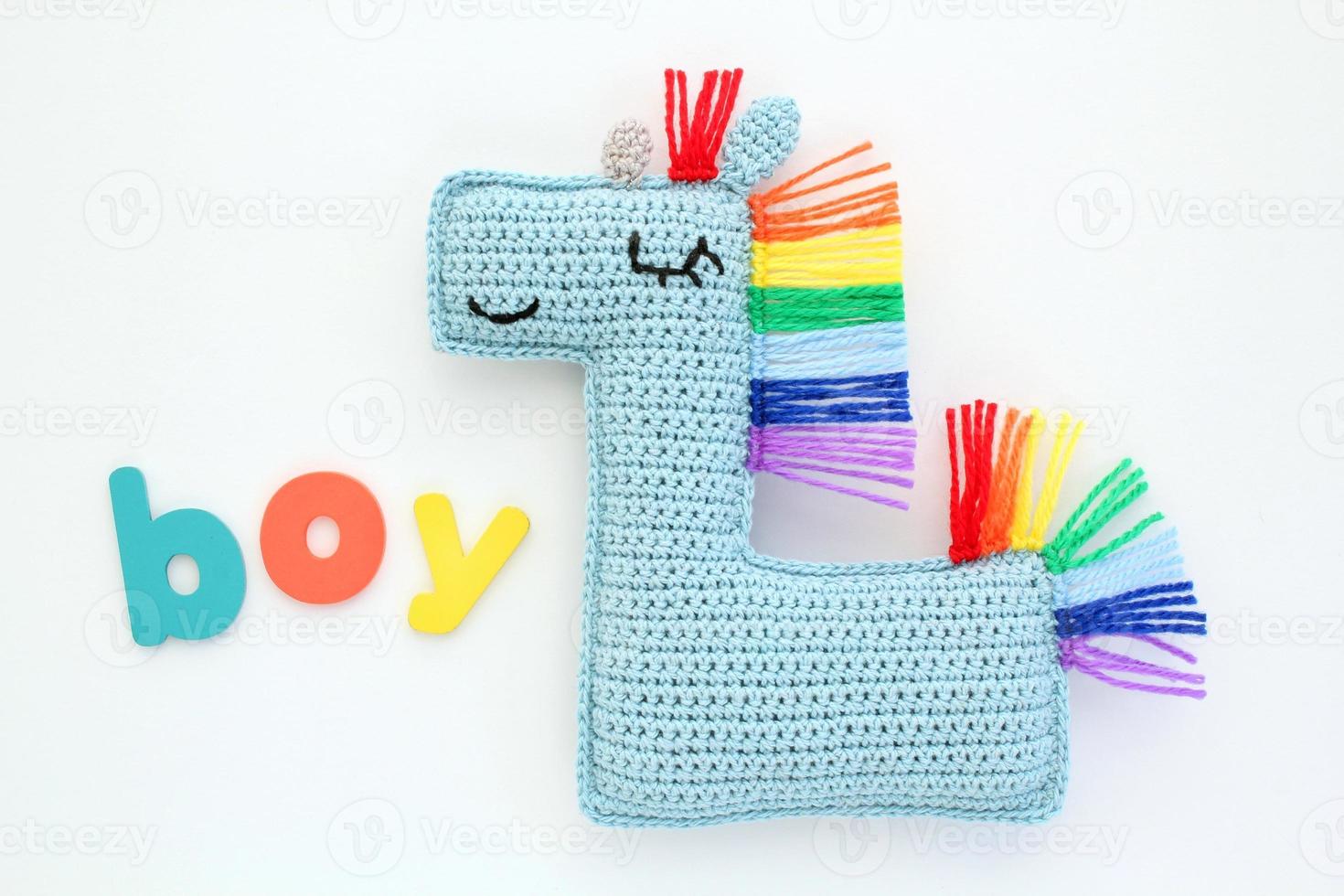 Crochet amigurumi handmade stuffed soft blue unicorn toy with rainbow mane and word Boy on white background. Handwork hobby. Craft diy newborn pregnancy concept. Knitted doll for little baby. Flat lay photo