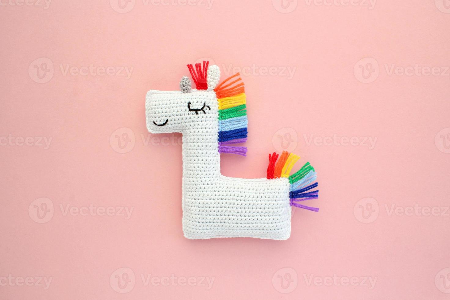 Crochet amigurumi handmade stuffed soft white unicorn toy with rainbow mane on pink background. Handwork, hobby. Craft diy newborn pregnancy concept. Knitted doll for little baby. Close up flat lay photo