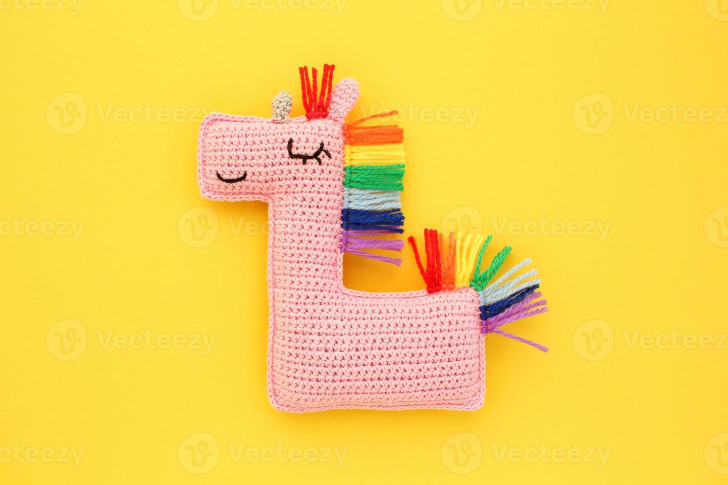 tejer amigurumi hecho a mano relleno suave rosado unicornio juguete con arco iris melena en amarillo antecedentes. trabajo manual, pasatiempo. arte bricolaje recién nacido el embarazo concepto. de punto muñeca para pequeño bebé. cerca arriba plano laico foto