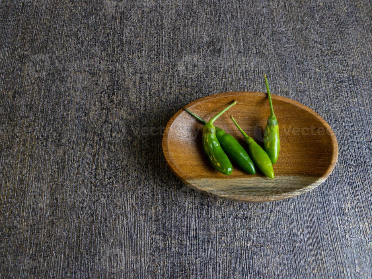 green chilli pepper or cabe rawit hijau in indonesian on a wooden plate. photo