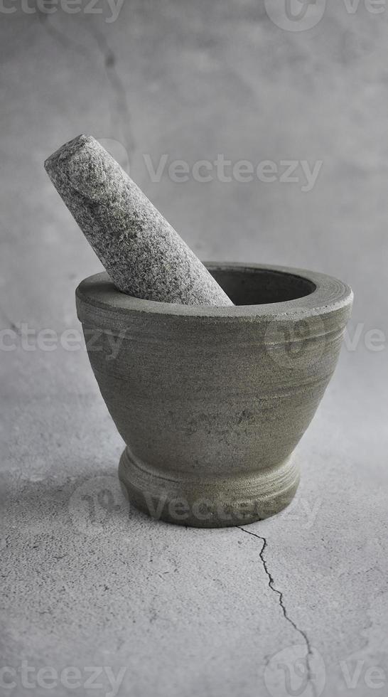 A side view of Thai granite stone mortar, grey color tone, with cracked cement floor background, same color, monochrome, kitchenware photo