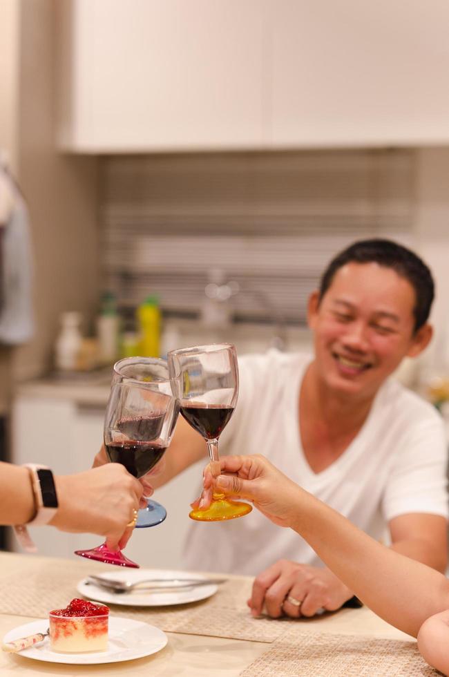 Asian man having a celebration with friends toasting glass of red at dinner party. photo