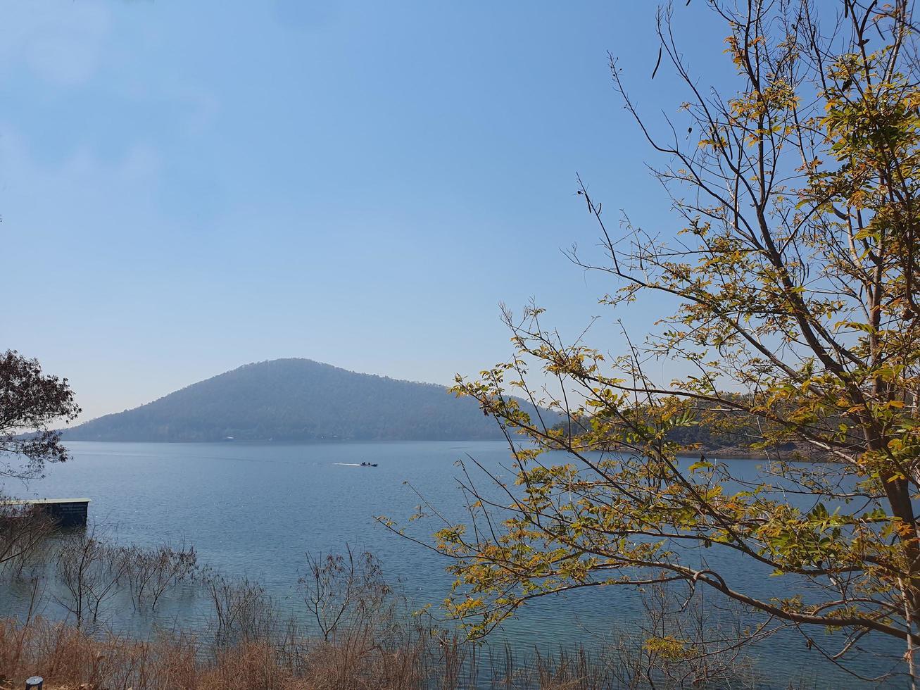 mountain view water reservoir summer yellow trees bright blue sky at noon and fishing boats of villagers in the water photo