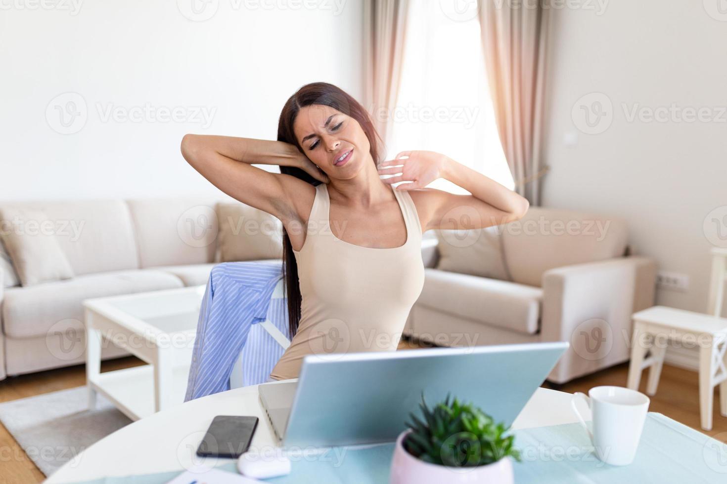 Waist up photo of young lady during a break sitting by the table and stretching her arms from hard work