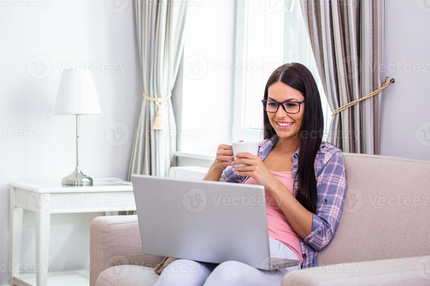 mujer joven positiva independiente viendo video en blog en netbook y tomando un café en casa cómoda. hermosa joven mujer de negocios trabajando en una laptop.freelancer conectándose a internet foto