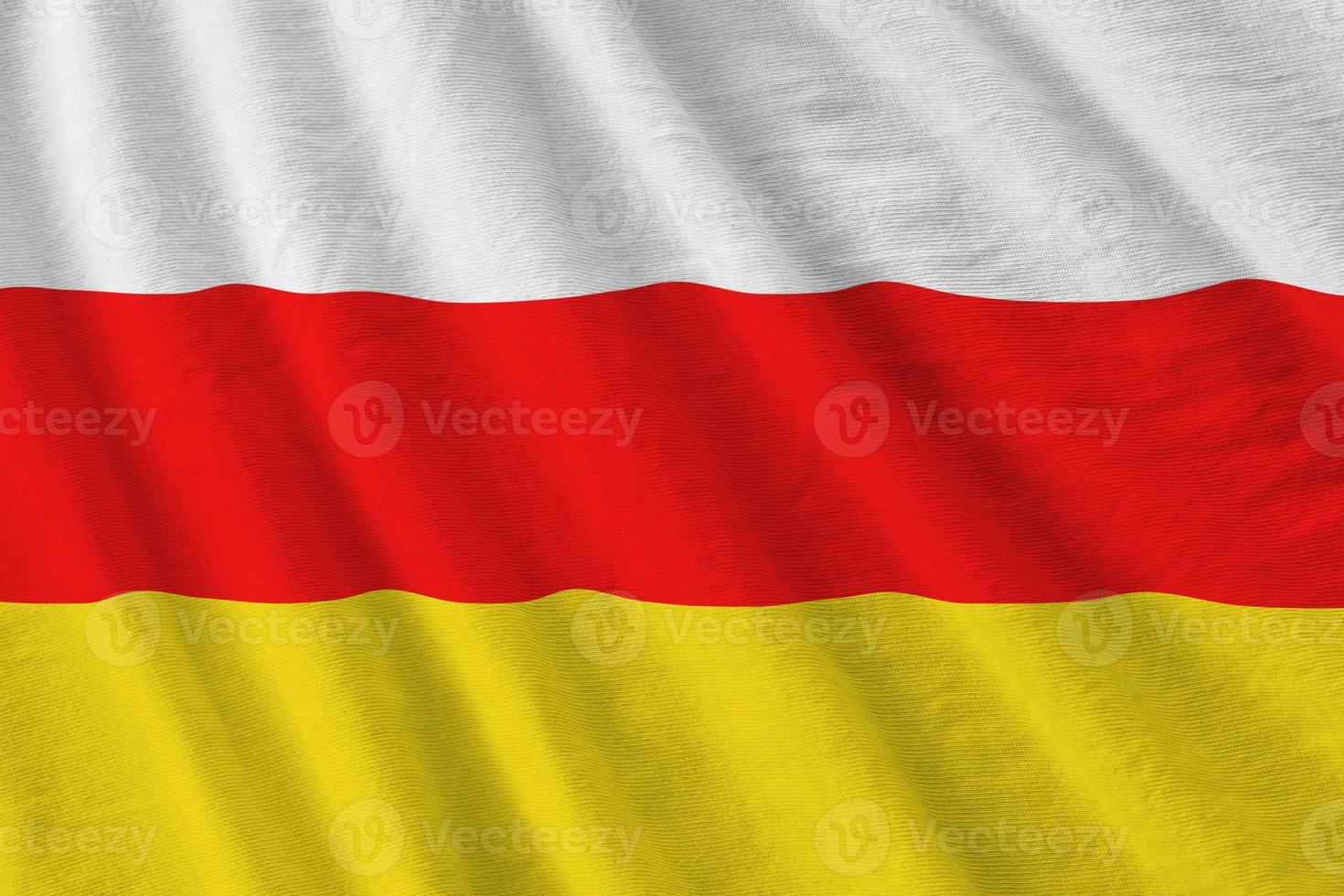 South Ossetia flag with big folds waving close up under the studio light indoors. The official symbols and colors in banner photo