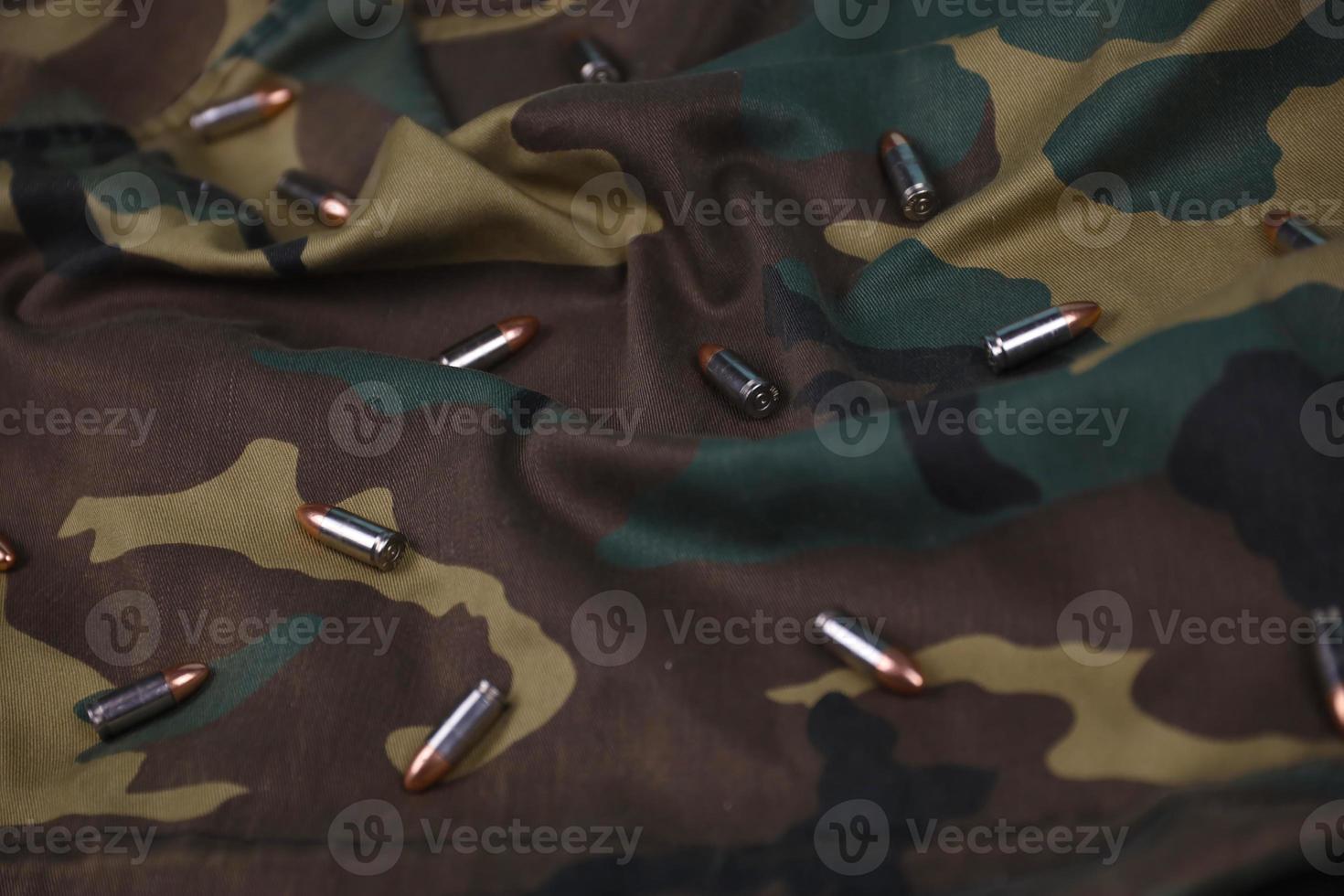 Many pistol bullets and cartridges on dark camouflage background photo