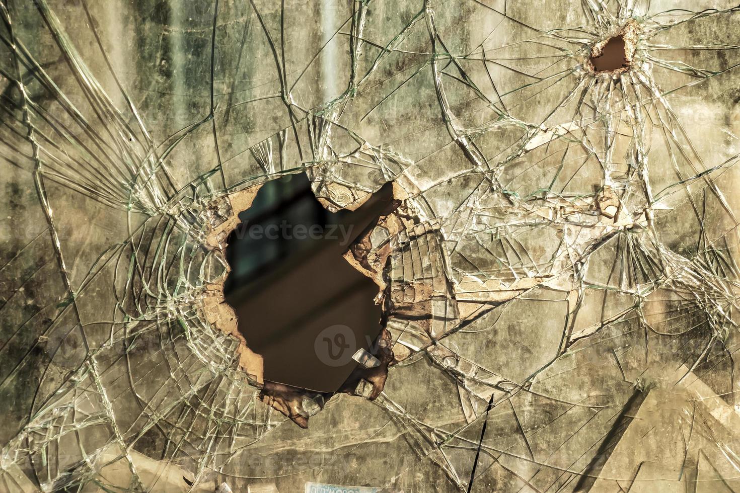 A hole in the window glass with a bullet during a military shooting. Cracks propagate around the hole. Dirty window frame. View of the street from the inside. photo