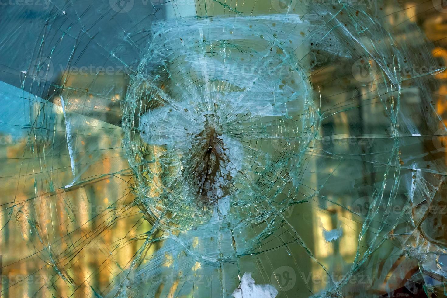 A hole in the window glass with a bullet during a military shooting. Cracks propagate around the hole. Dirty window frame. View of the street from the inside. photo