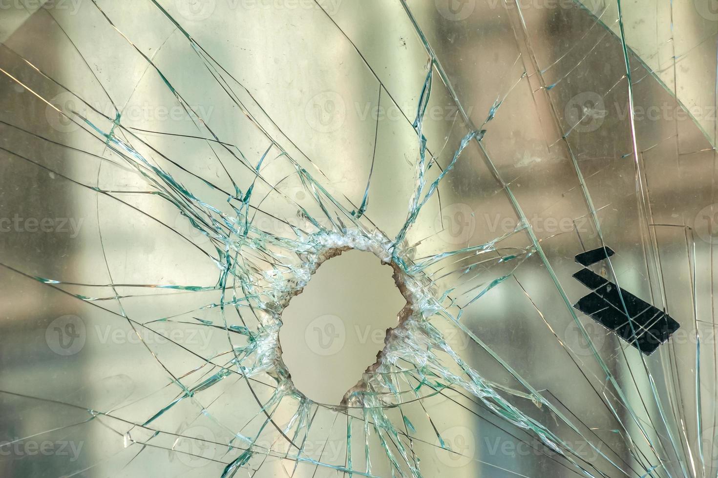 A hole in the window glass with a bullet during a military shooting. Cracks propagate around the hole. Dirty window frame. View of the street from the inside. photo