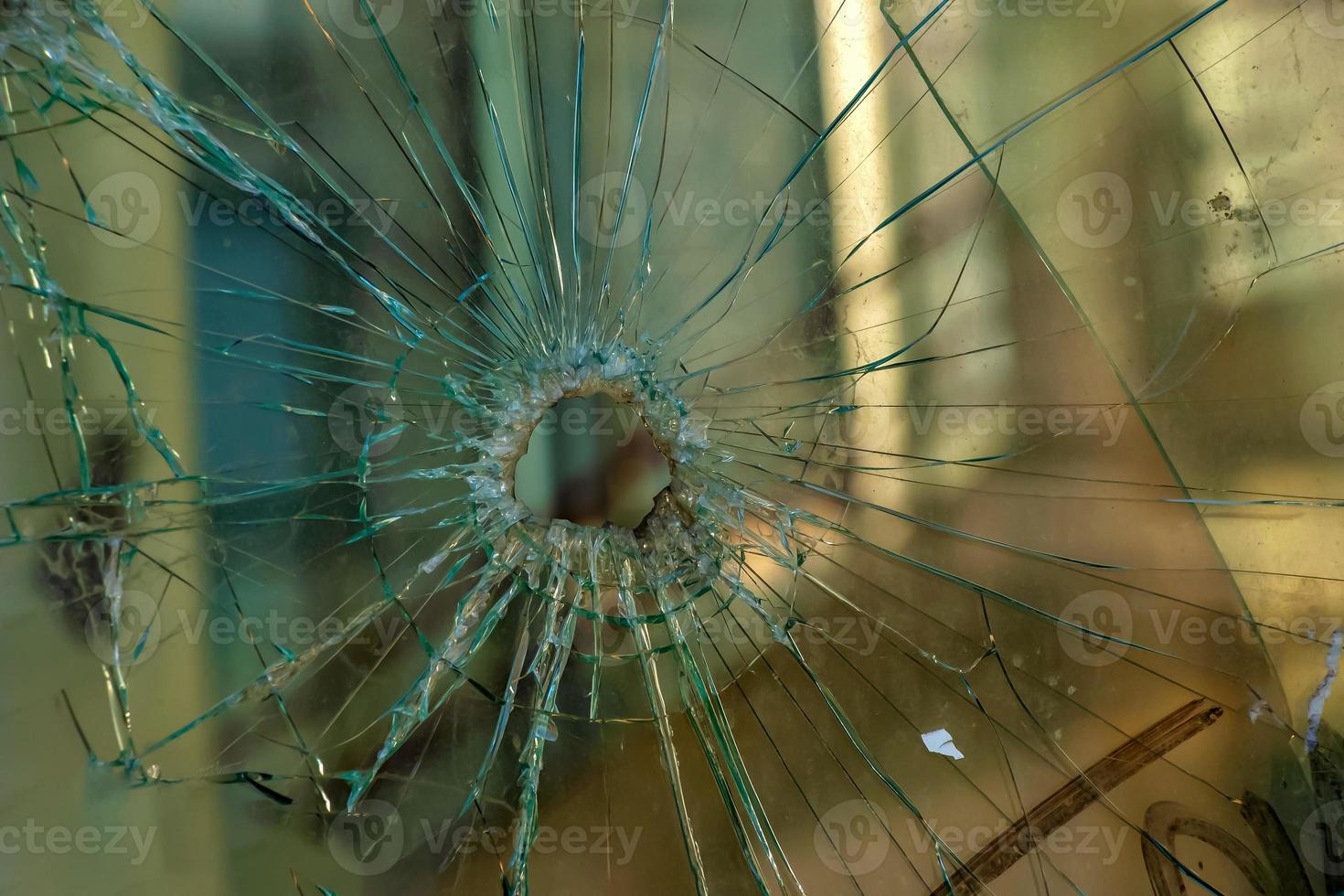 A hole in the window glass with a bullet during a military shooting. Cracks propagate around the hole. Dirty window frame. View of the street from the inside. photo