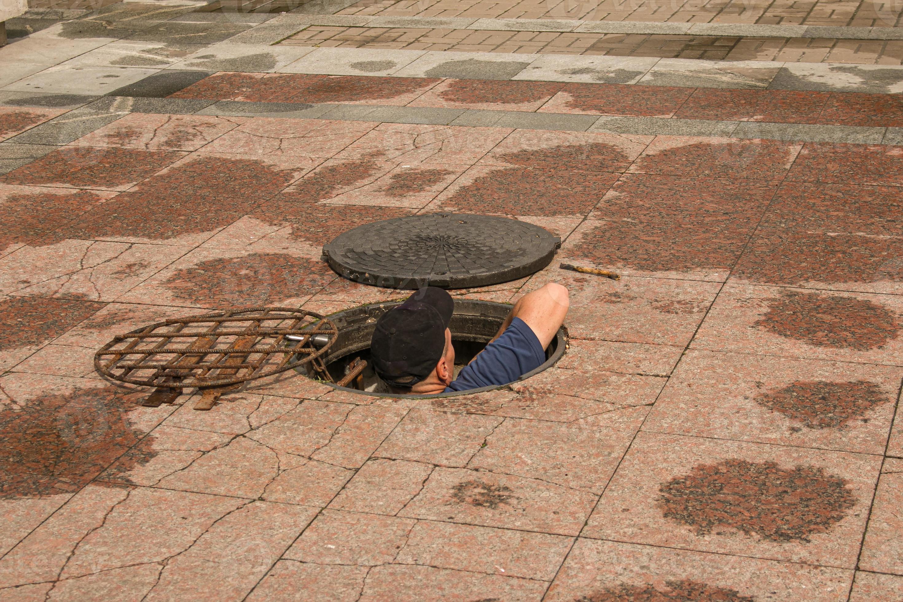 A worker climbs out of an open manhole in the road A worker climbs out of an open manhole in the road