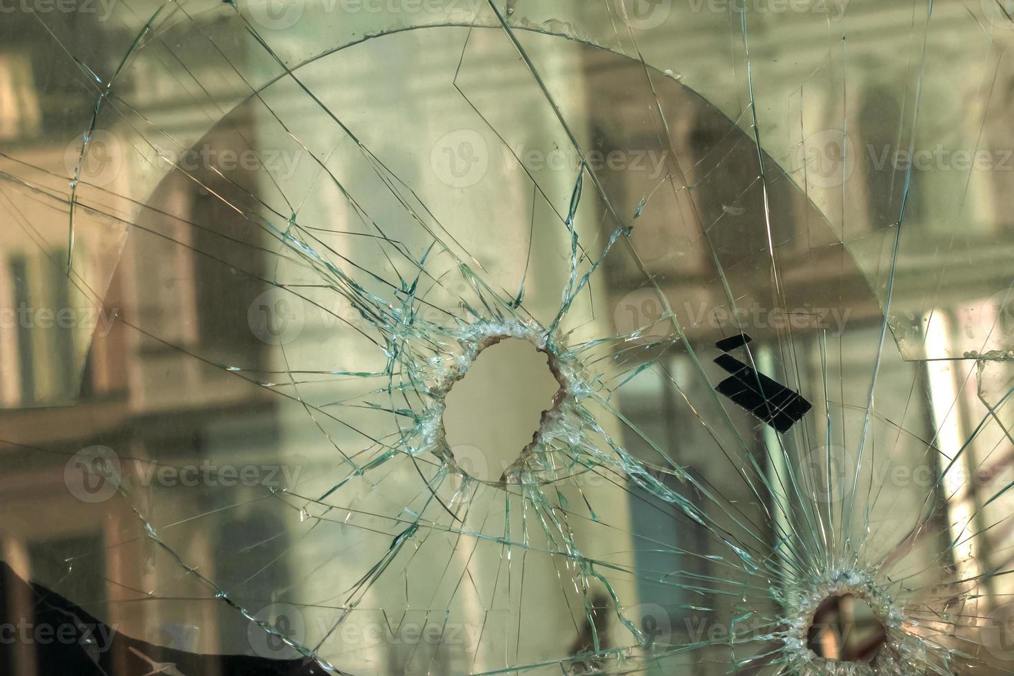 A hole in the window glass with a bullet during a military shooting. Cracks propagate around the hole. Dirty window frame. View of the street from the inside. photo