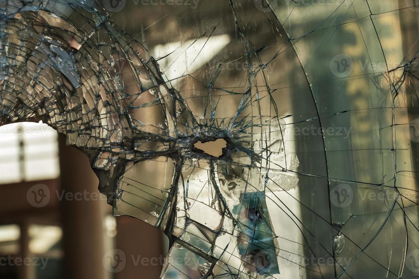 A hole in the window glass with a bullet during a military shooting. Cracks propagate around the hole. Dirty window frame. View of the street from the inside. photo