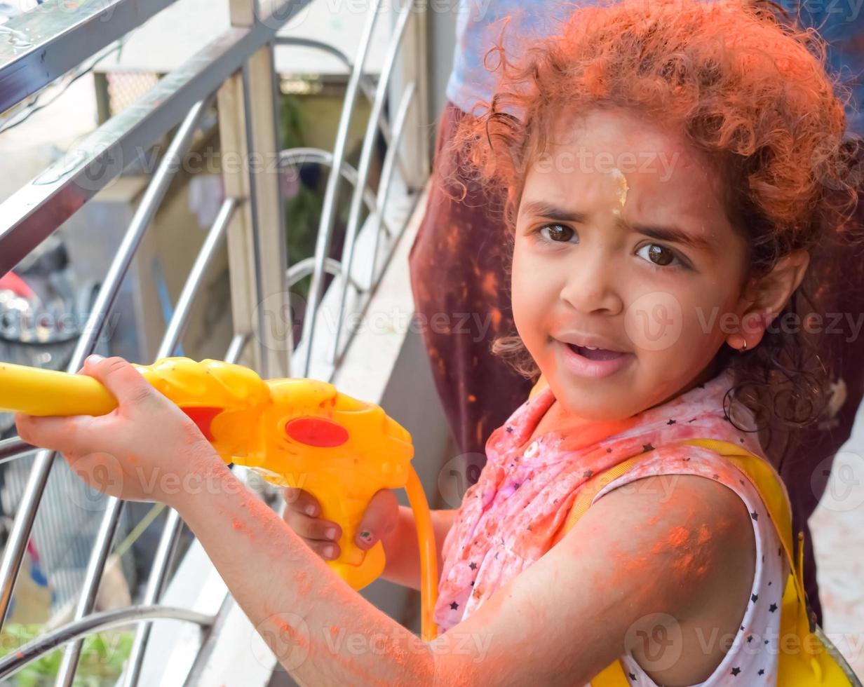 dulce pequeño indio niña jugando colores en holi festival, participación pichakaree lleno de colores, holi festival celebraciones en Delhi, India foto