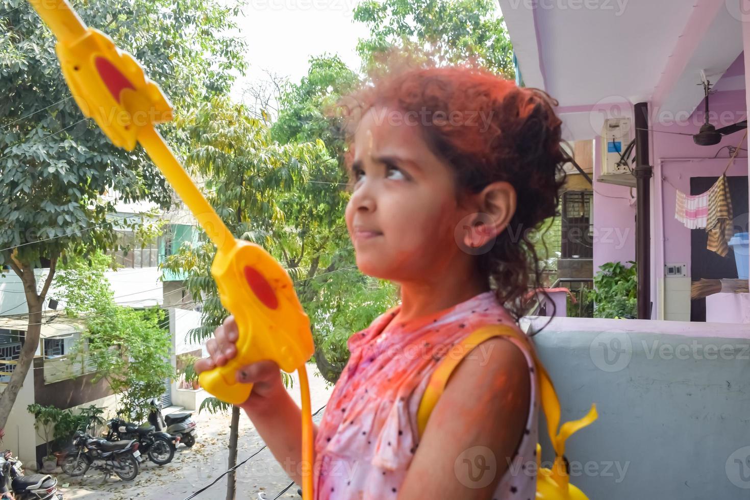 Sweet little Indian girl playing colours on Holi festival, holding pichakaree full of colours, Holi festival celebrations in Delhi, India photo