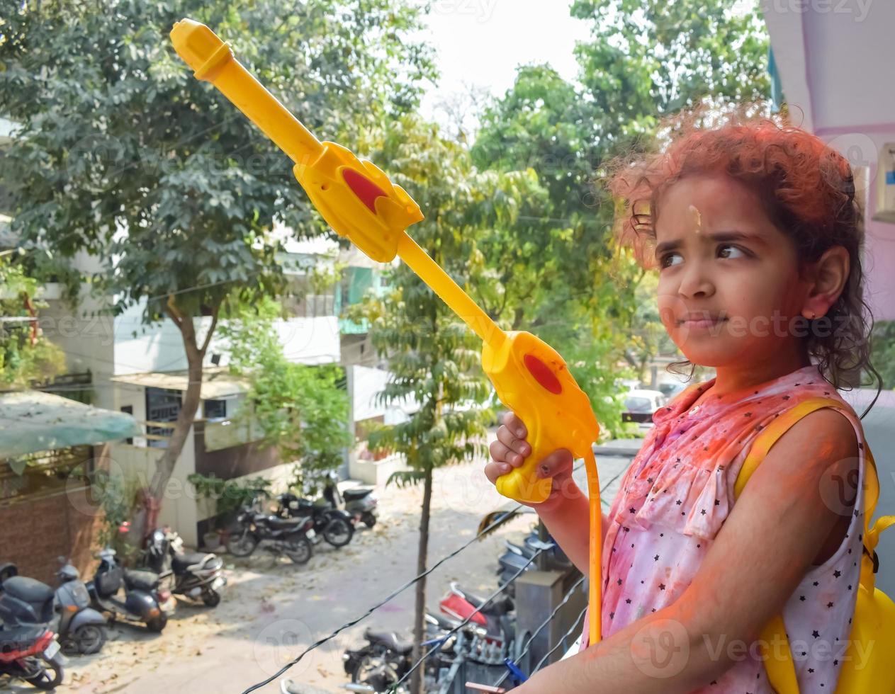 dulce pequeño indio niña jugando colores en holi festival, participación pichakaree lleno de colores, holi festival celebraciones en Delhi, India foto