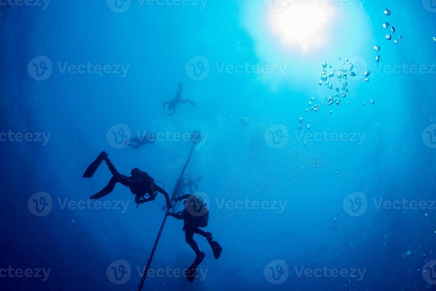 divers under boat for deco time in the blue photo