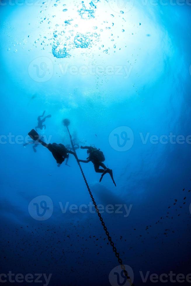 divers under boat for deco time in the blue photo