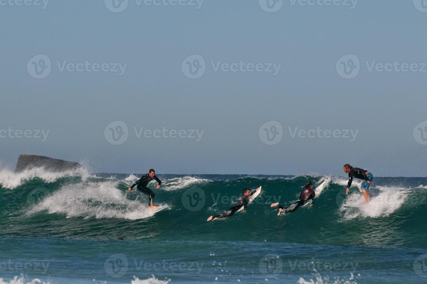 A group of four surfers jumping and riding on big waves photo