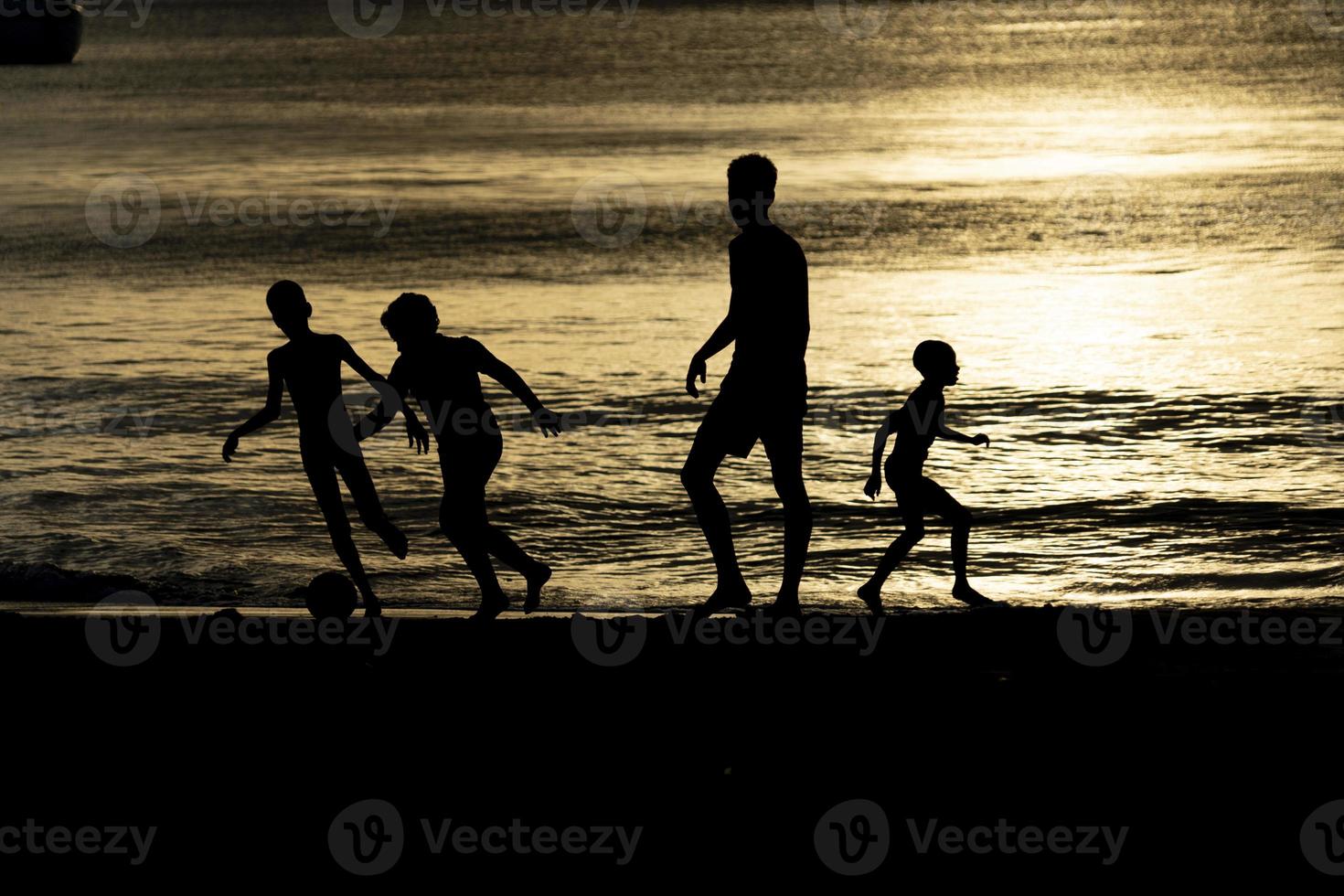 silhouette of black childrens playing soccer at the beach at sunset photo