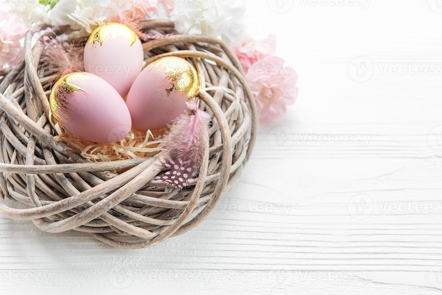 Easter eggs painted pink and gold and  feathers in a nest on a white wooden background. photo