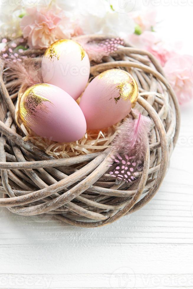 Easter eggs painted pink and gold and  feathers in a nest on a white wooden background. photo