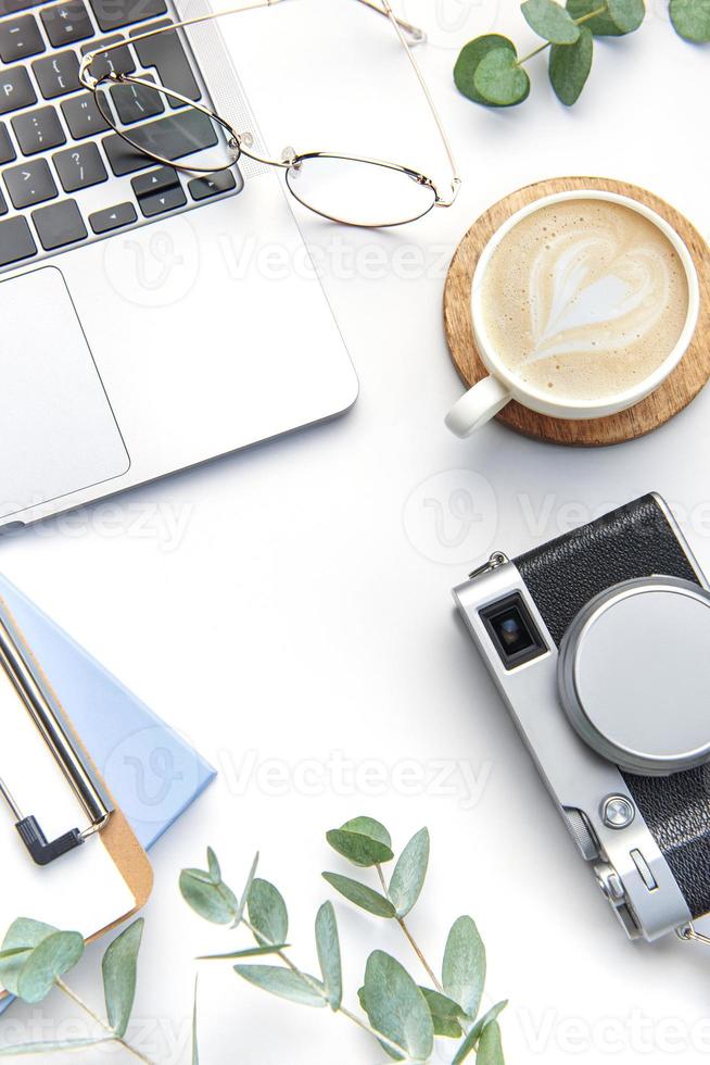 Modern white office desk table with laptop, camera, notebook and other supplies. photo