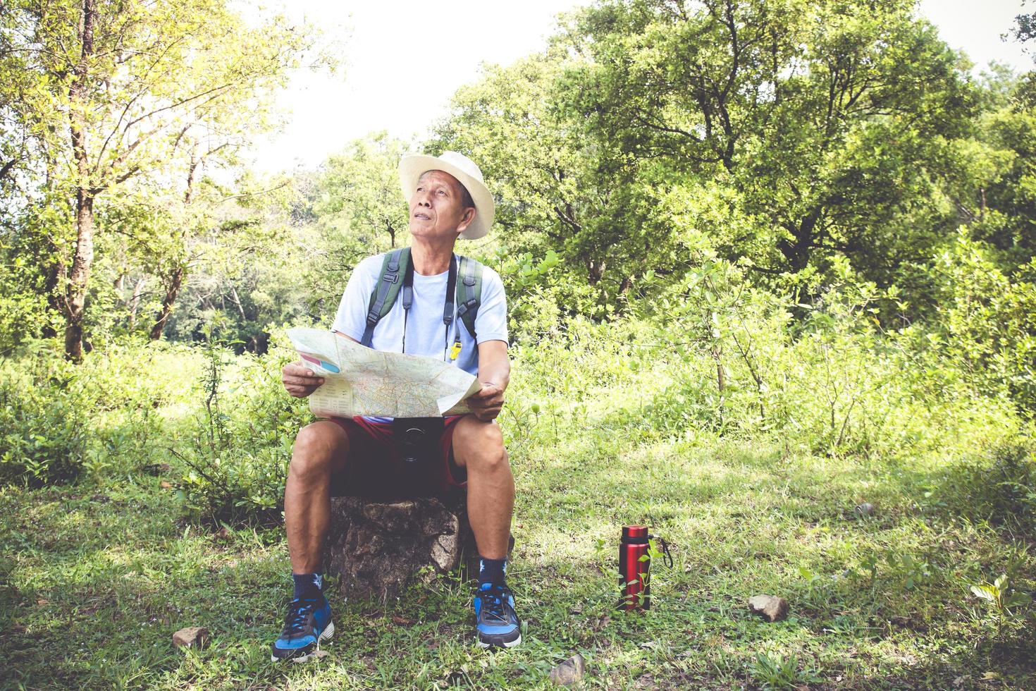 hombre mayor mochilero senderismo abre un mapa de papel para estudiar la ruta turística natural. el concepto de vida feliz después de la jubilación. con espacio de copia. foto