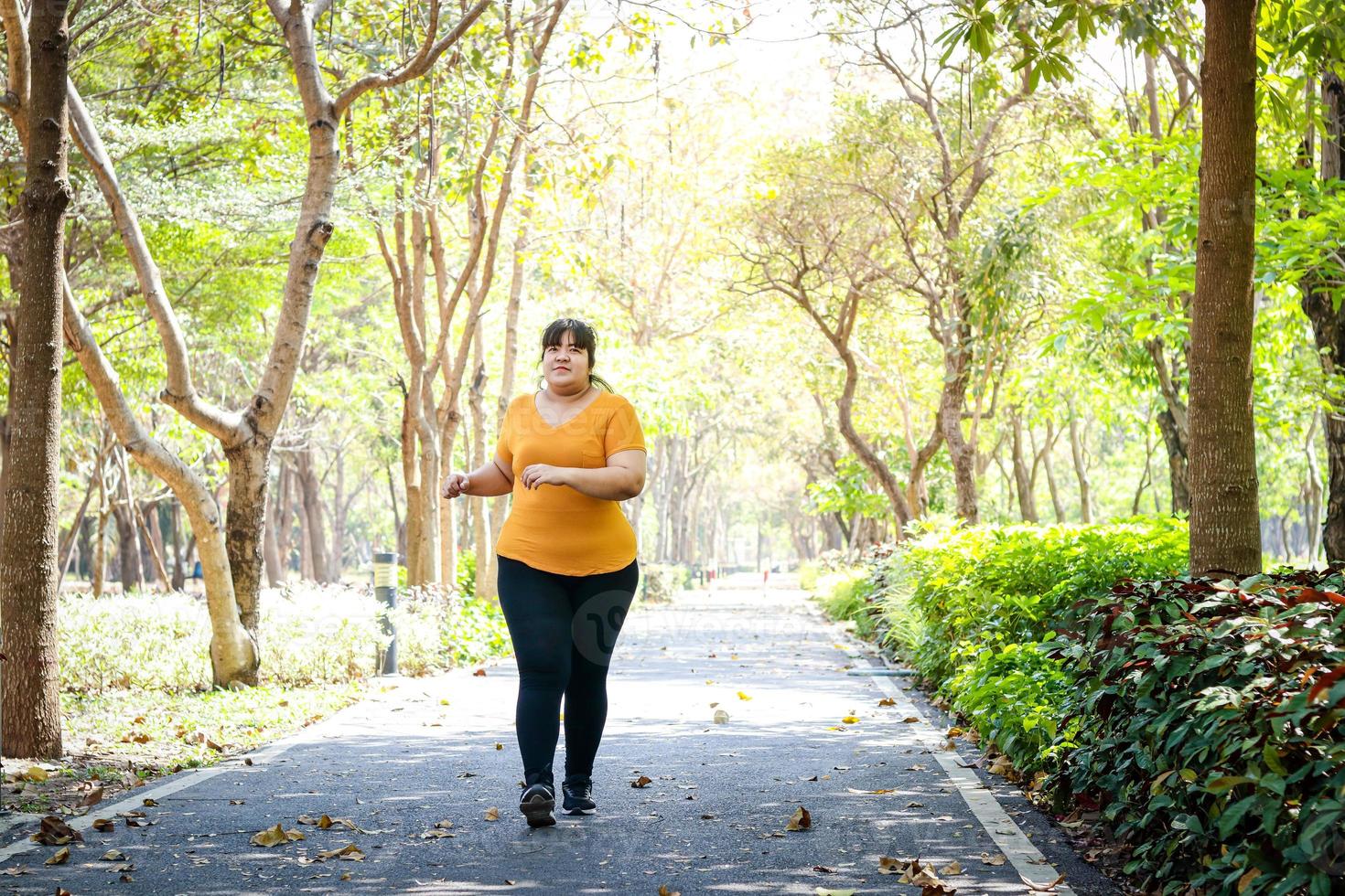 Fat Asian woman wearing yellow blouse Jogging in the morning In the park. Concept of weight loss Exercise for the good health of obese people. Copy space photo
