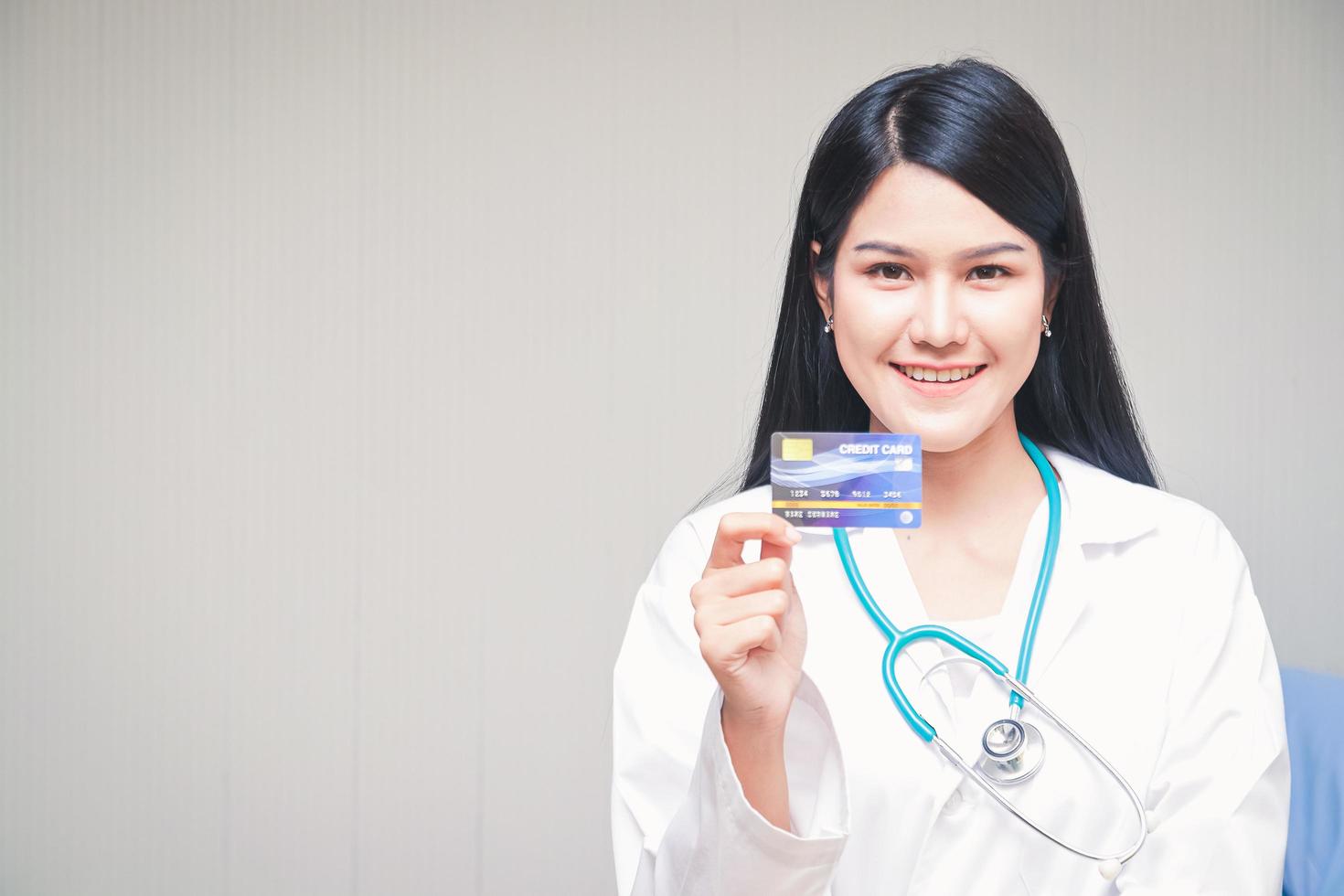 hermosa asiático médico participación un crédito tarjeta en pie sonriente brillantemente blanco fondo. salud Servicio concepto y Finanzas en uno tarjeta foto