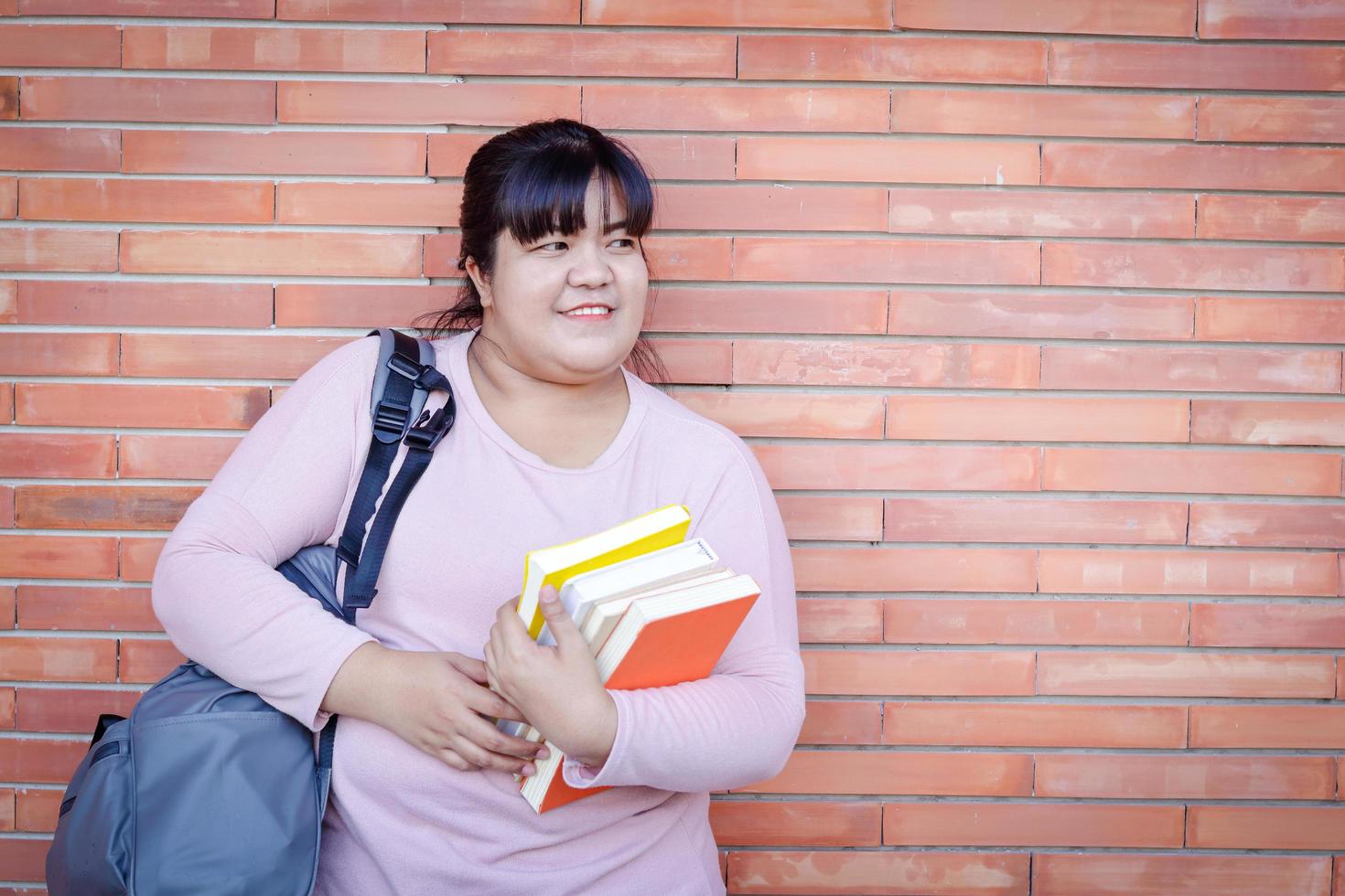 un grasa asiático mujer que lleva un libro de texto y que lleva un bolsa. concepto de adulto educación personal desarrollo y aprendiendo. Copiar espacio foto