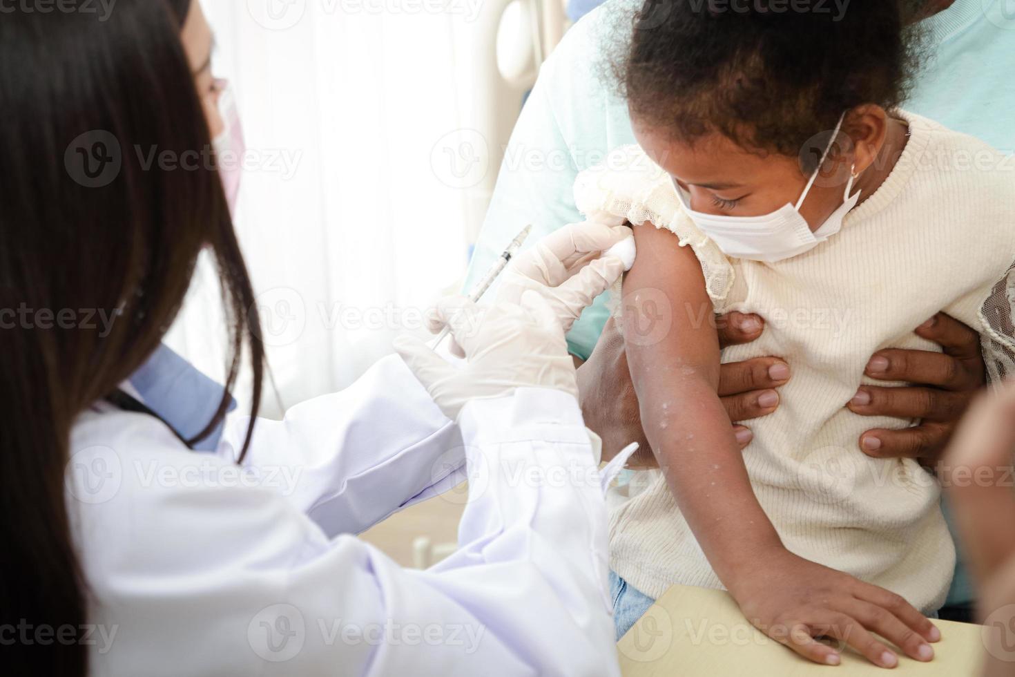 Doctors inject a vaccine in the arm of a young African-American girl to strengthen immunity and protect it from diseases. Concept of the vaccine against COVID-19. Medical services in hospitals. photo