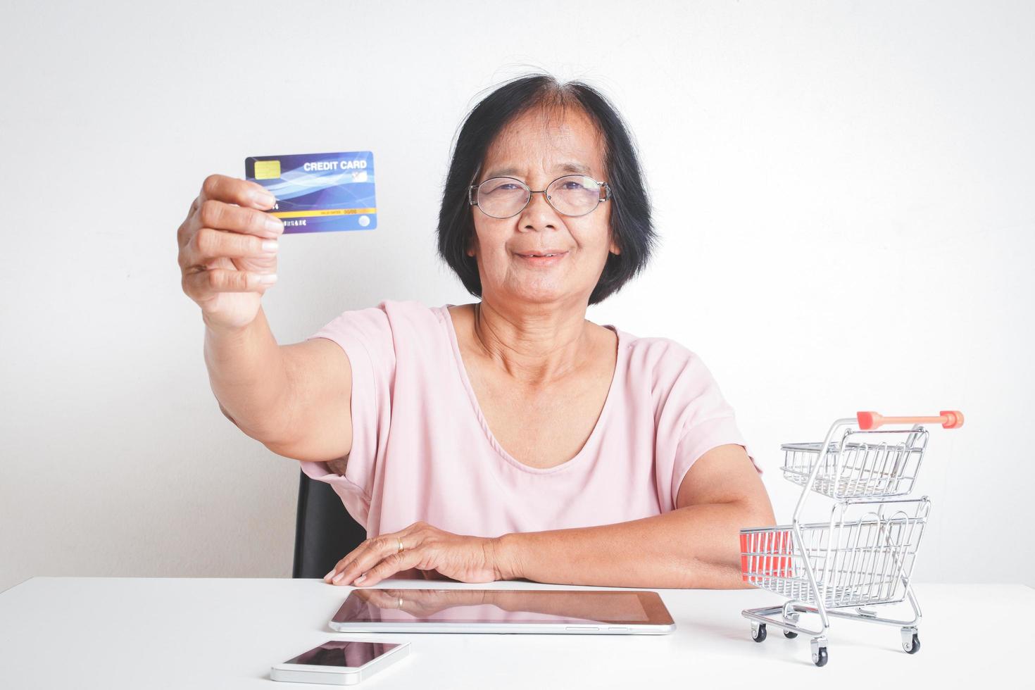 asiático más viejo mujer participación burlarse de arriba crédito tarjetas, mano prensado tableta pantalla comprar productos en línea. mayor comunidad conceptos foto