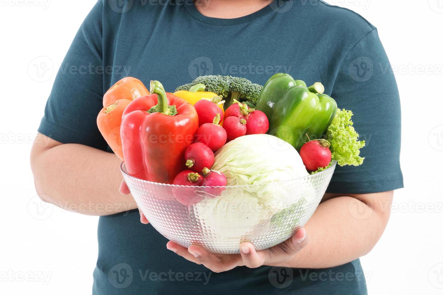 A fat woman holds fresh organic vegetables in a clear glass bowl. The concept of losing weight Eat healthy foods. White background photo