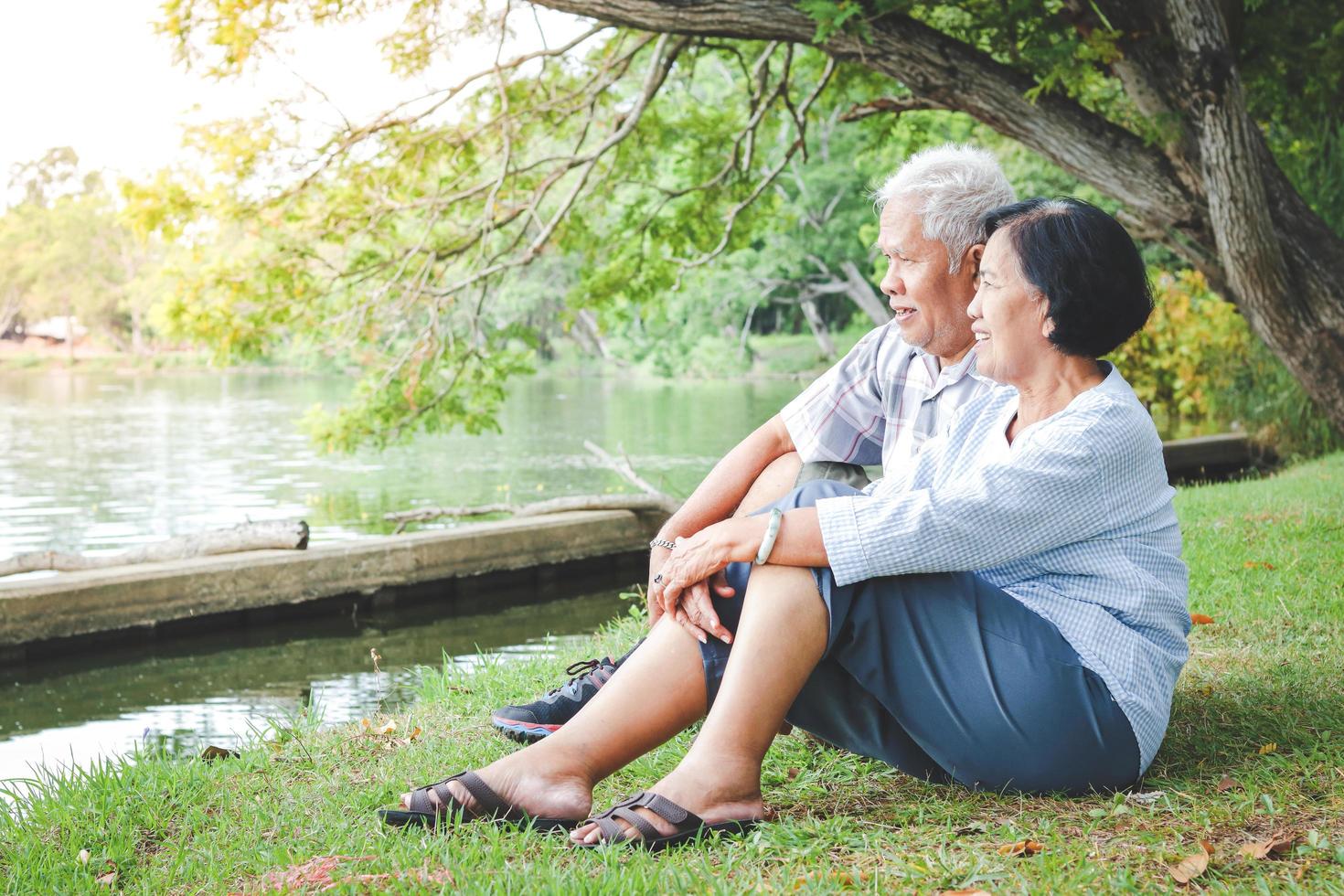 An elderly couple hugging each other with love and happiness in a park with a large pond. Senior community concept, good health, longevity photo