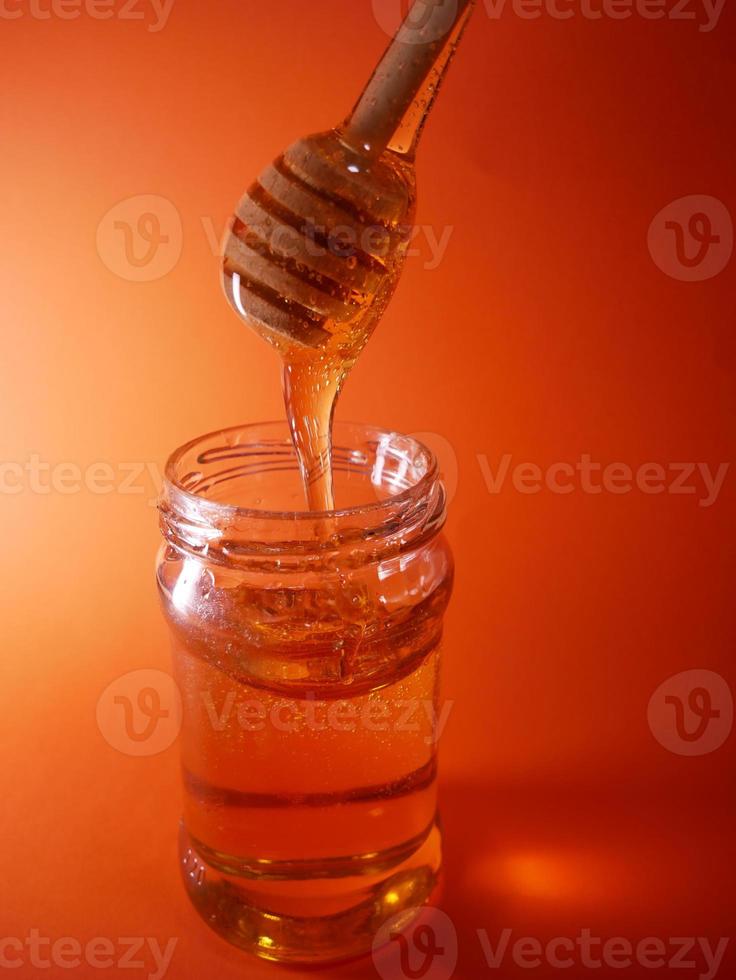 Honey jar with spindle spoon on orange background photo