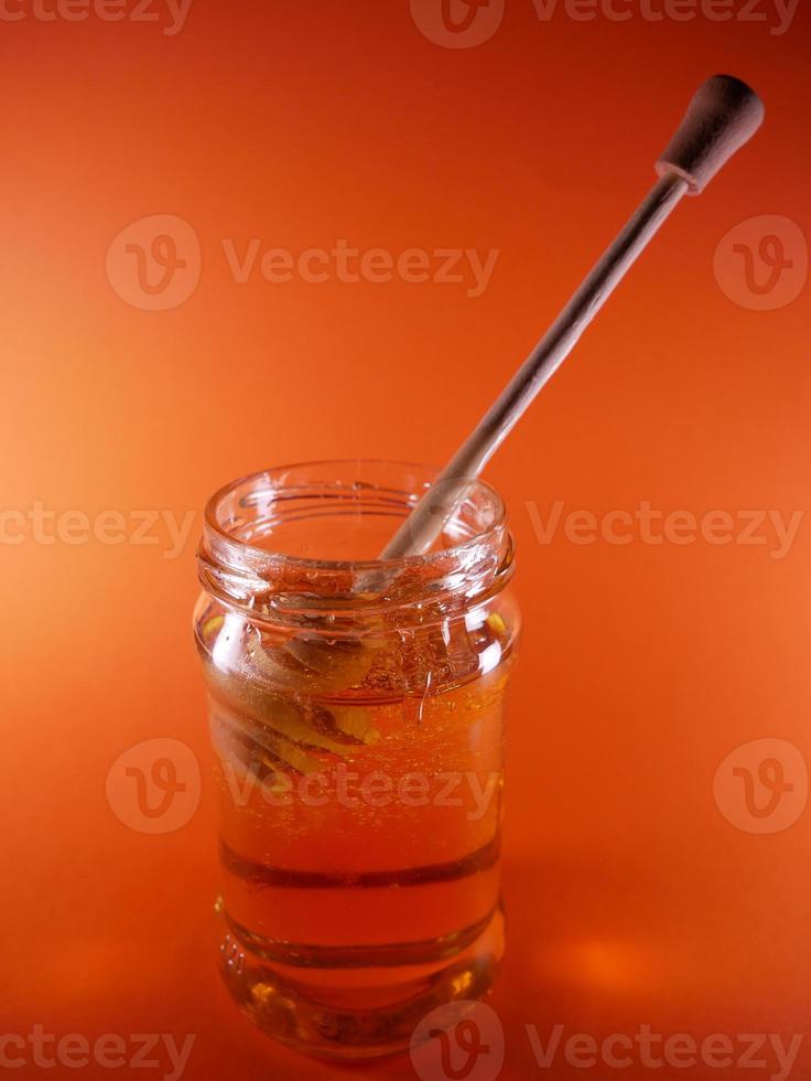 Honey jar with spindle spoon on orange background photo