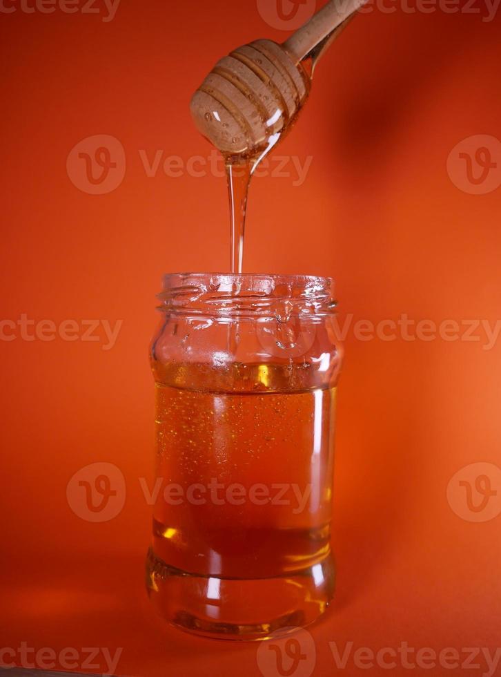 Honey jar with spindle spoon on orange background photo