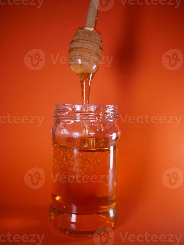 Honey jar with spindle spoon on orange background photo